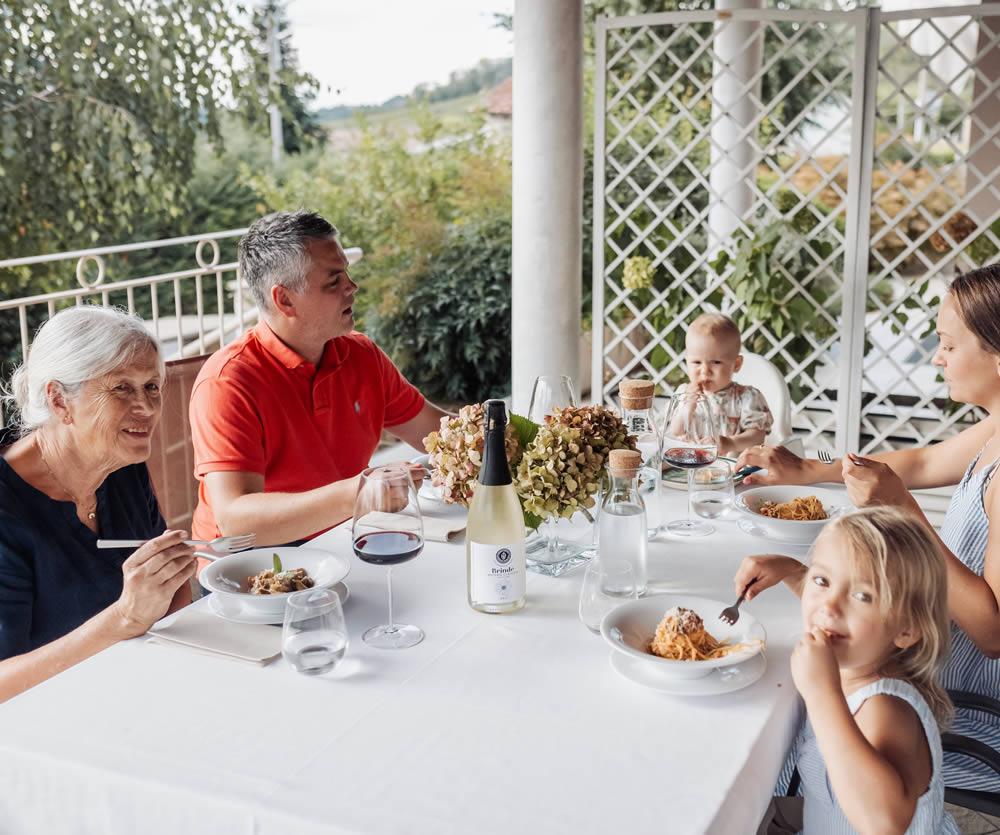 Famiglia cena all'aperto, piatti di pasta, vino e atmosfera serena.