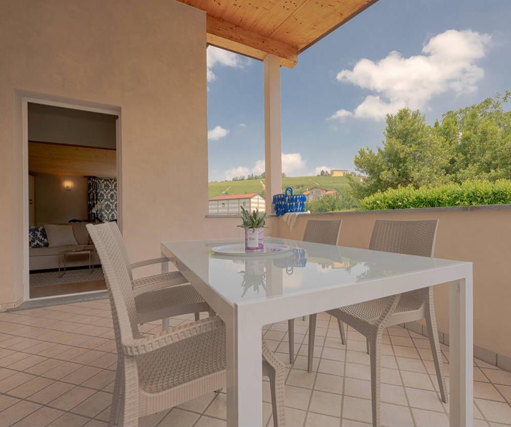 Terrazza con tavolo bianco, sedie e vista su colline verdi.