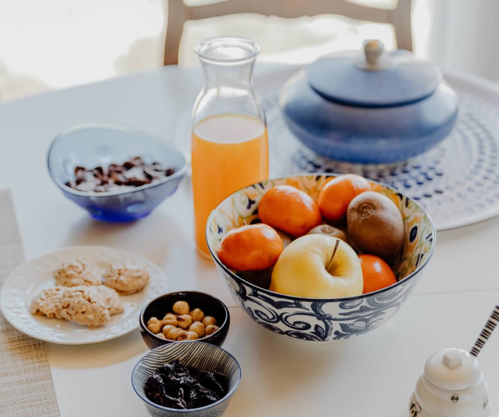 Colazione con frutta, biscotti, nocciole e succo d'arancia su tavola apparecchiata.