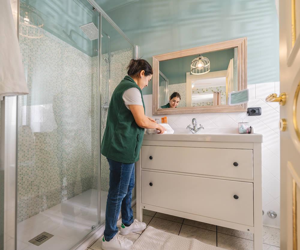 Persona pulisce il bagno, con doccia e specchio, in un ambiente luminoso.