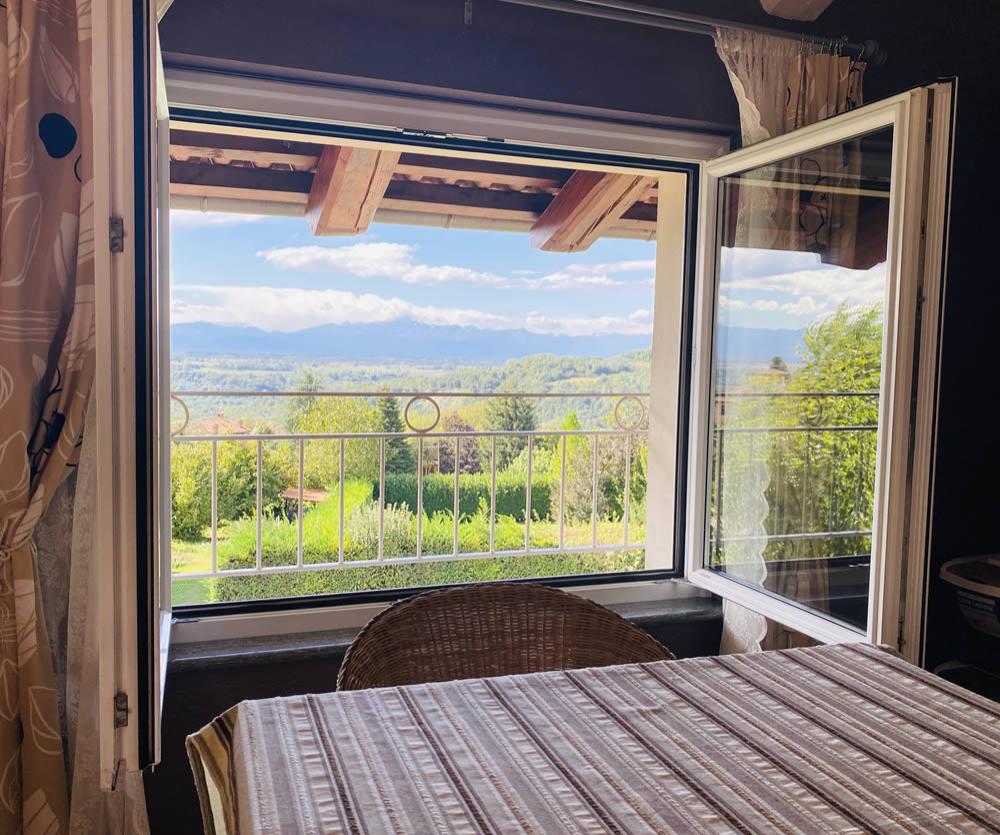 Vista panoramica dalla finestra su colline verdi e cielo azzurro.