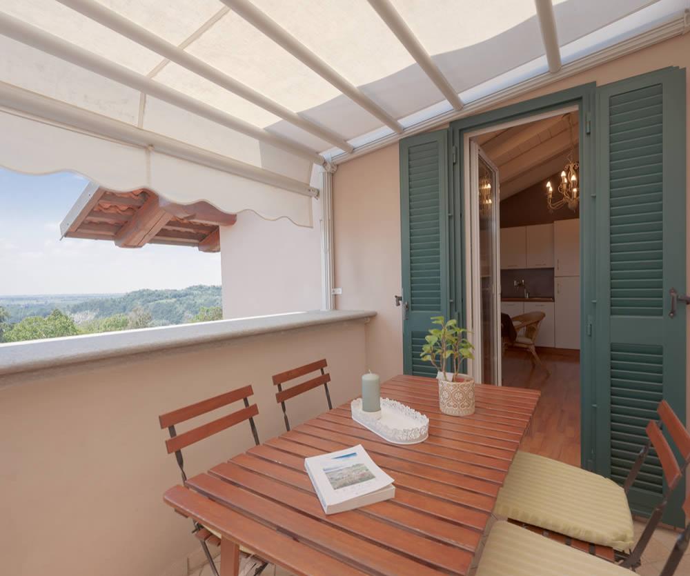 Terrazza con tavolo in legno, vista panoramica, tende da sole e accesso alla cucina.