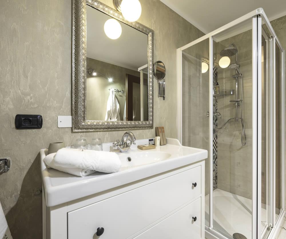 Elegante bagno con doccia moderna, specchio decorato e lavabo bianco con asciugamani.