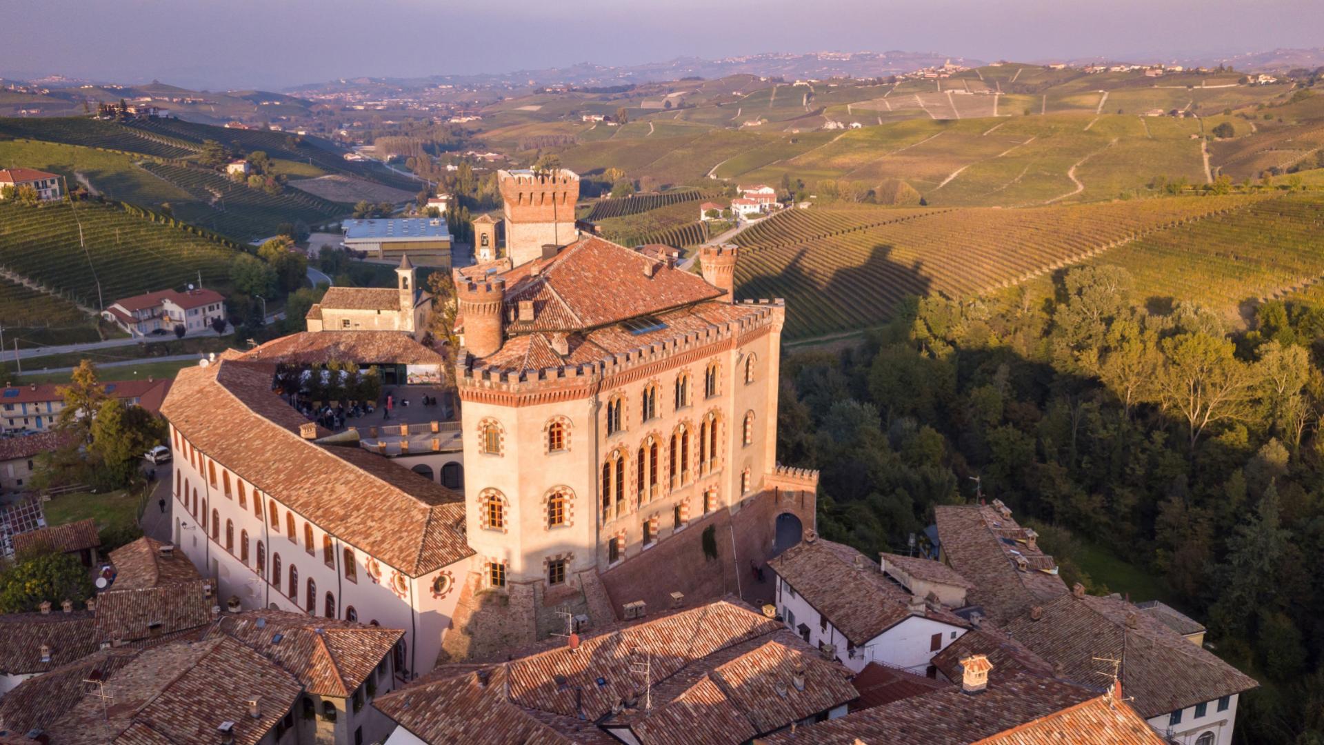 Castello medievale circondato da vigneti e colline al tramonto.