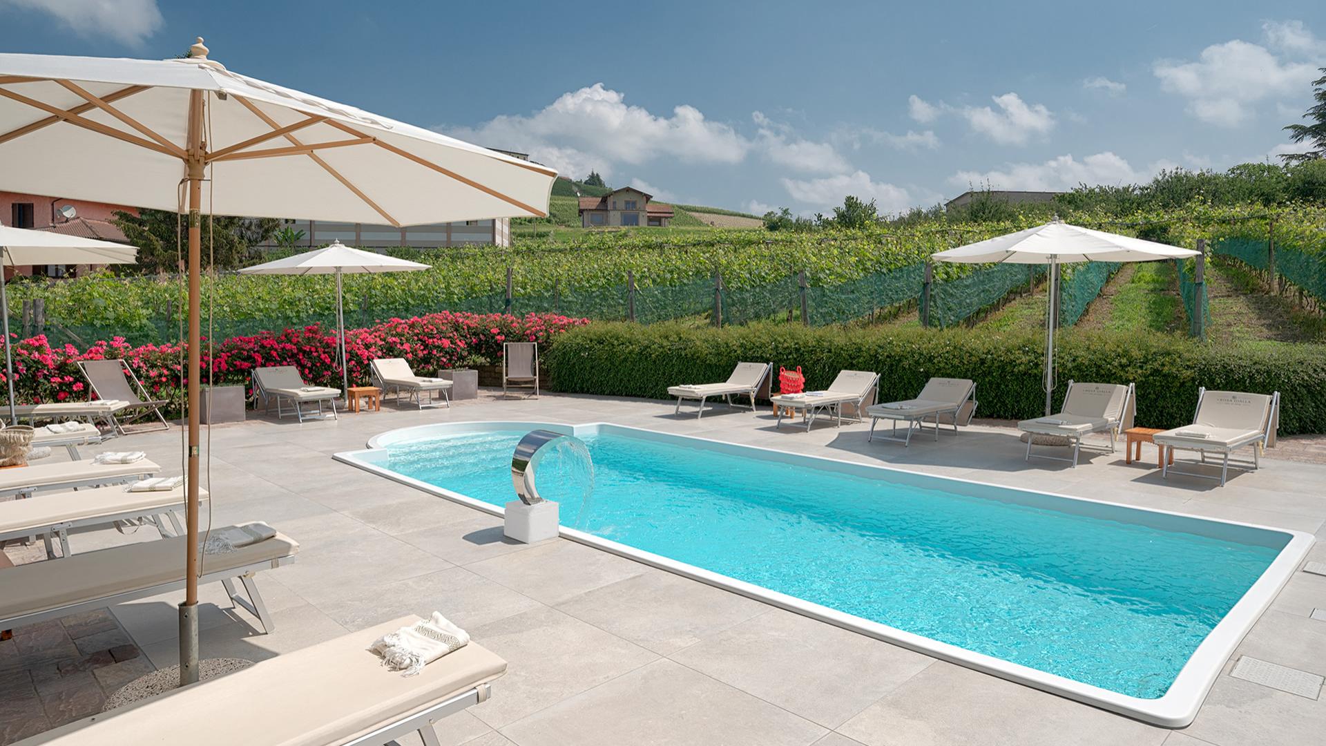 Piscina con vista su vigneti, lettini e ombrelloni in una giornata soleggiata.